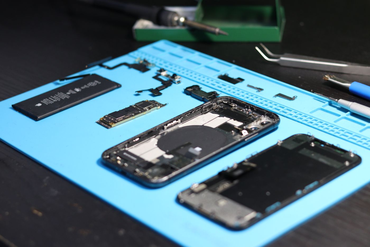 Rozłożony smartfon i narzędzia na niebieskiej macie serwisowej