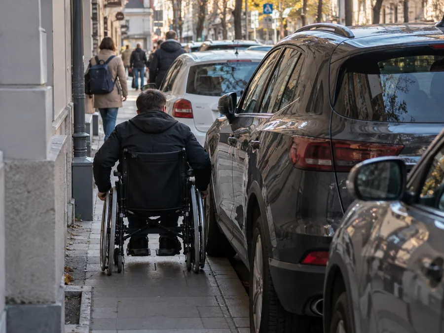 Osoba poruszająca się na wózku napotyka samochody zastawiające chodnik w mieście